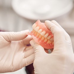 Hands in white gloves holding a complete set of dentures